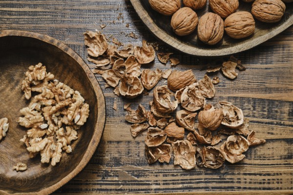 Whole walnuts and broken shells scattered across a wooden table. Some walnut pieces are neatly