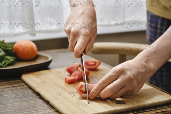 Hands skillfully slice fresh tomatoes on a wooden cutting board while preparing a delicious meal in