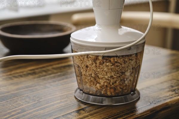 Chopping walnuts in a food processor on a rustic wooden table. The device is plugged in and the