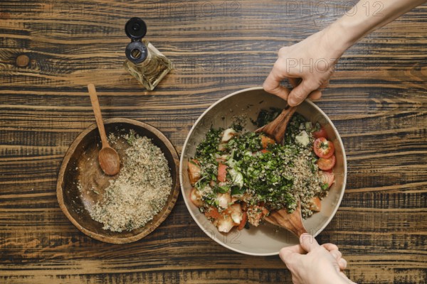 Hands gently mix fresh tomatoes, herbs, and chopped walnuts in a large bowl. Wine vinegar oil is