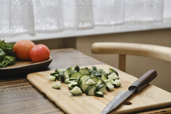 Freshly chopped cucumbers on a wooden cutting board beside a knife. A bowl of tomatoes is visible