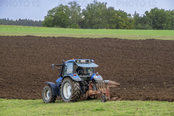 Tractor with plough, agricultural ploughing machine working on a field in autumn, fall in the