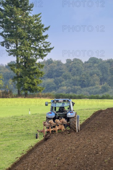 Tractor with plough, agricultural ploughing machine working on a field in autumn, fall in the