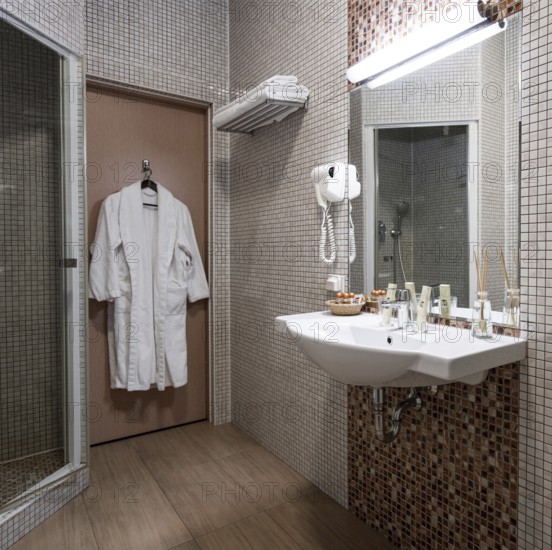 Fine hotel bathroom interior in beige color with bathrobe hanging on the door