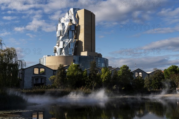 Front lake with artificial fog, Luma, 56 m high irregular tower designed by Frank Gehry, tower in