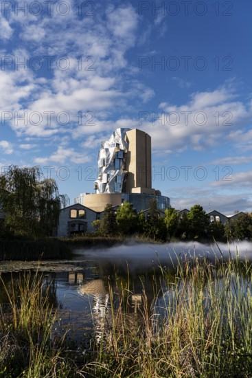 Front lake with artificial fog, Luma, 56 m high irregular tower designed by Frank Gehry, tower in