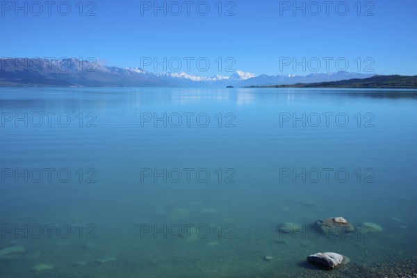 Clear, calm lake in front of a distant mountain range under blue sky, Lake Pukaki Viewpoint,