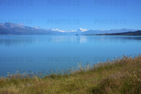 View over grassy banks to the mountain range behind the lake, Lake Pukaki Viewpoint, Pukaki,