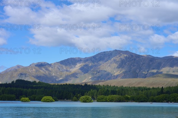Mountainous landscape with a lake in the foreground and wooded hills under a cloudy sky, Lake