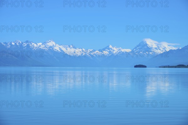 Mount Cook snow-capped mountains are reflected in a calm, blue lake, Lake Pukaki Viewpoint, Pukaki,