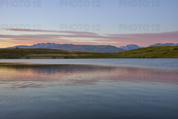 Clear lake with mountains in the background under a pink-blue morning sky, Lake McGregor, Tekapo,