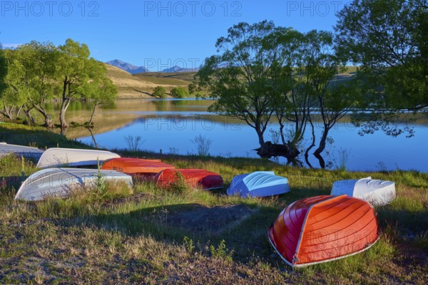 Boats on the shore of a calm lake at dusk with reflecting mountains in the background, Lake