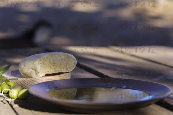 Extra virgin olive oil in a bowl, bread, and green olives on a rustic wooden table capturing