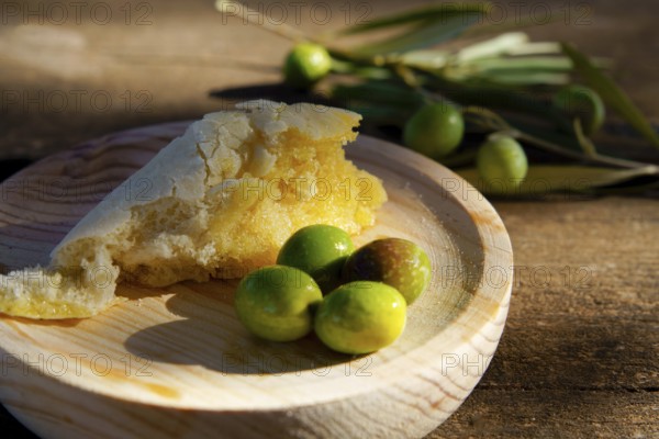 Rustic bread dipping in extra virgin olive oil served with fresh green olives on a wooden
