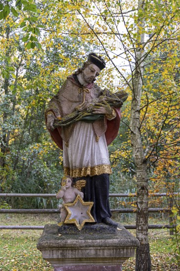 Religious statue with cape and angel in an autumnal park in front of yellow leaves, Weinviertel