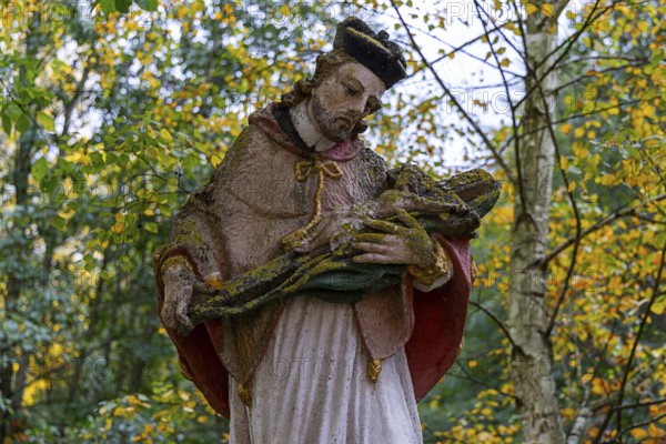 Close-up of a religious statue with a cape in an autumnal park, covered by moss, Weinviertel Lower