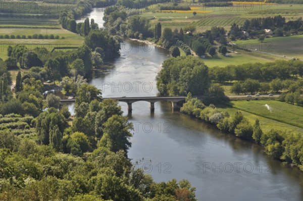 An aerial view of a serene river flowing under a bridge, surrounded by lush green fields and trees.