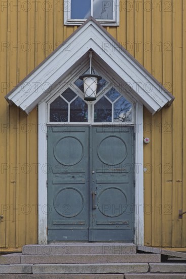 Closed old decorative double doors with white frame and window on top on a yellow board wall,