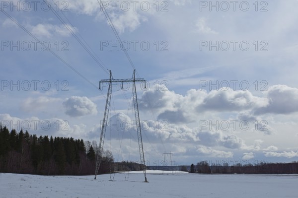 Steel tower with high voltage electric lines in cloudy winter weather with snow on the ground,
