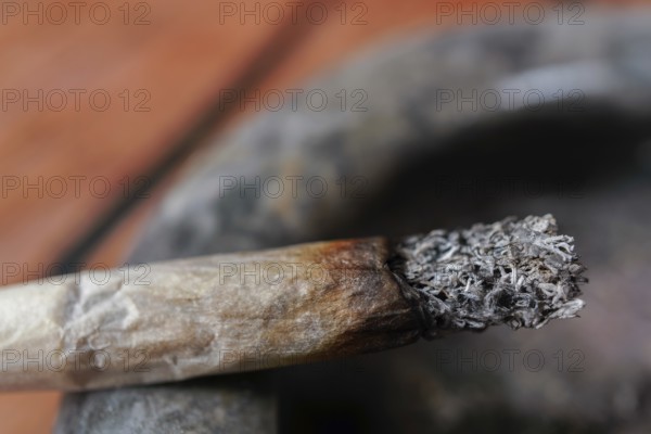 Close-up of a burning cigarette with a long ash resting on a dirty ashtray, symbolizing an
