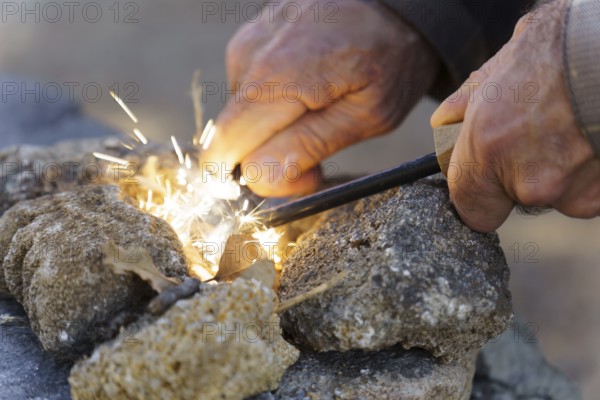 Bushcraft survivalist creating fire sparks with a ferro rod and cotton tinder, gathering heat