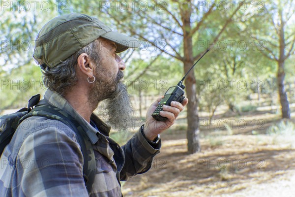 Man with beard and cap holding a walkie-talkie, communicating during an outdoor activity in a