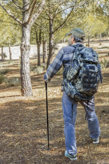 Man walking an outdoor path, carrying a camouflage backpack and trekking pole, enjoying nature and