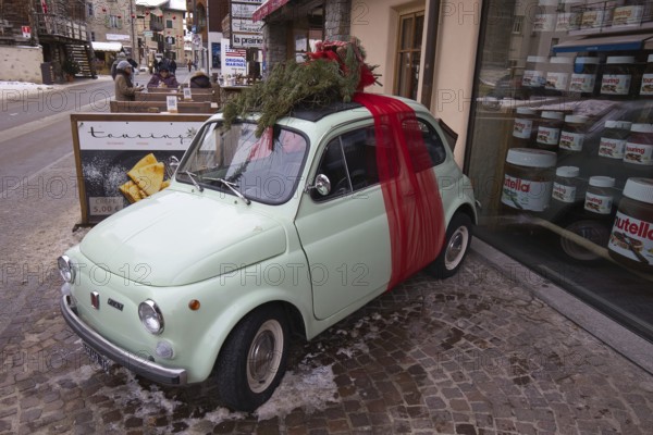 In Livigno in Lombardy in Italy, a small vintage Fiat, decorated as a Christmas present, stands in