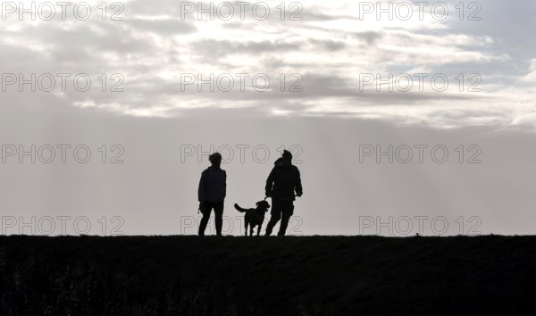 Couple with dog walking across a dike on the Baltic Sea, Fehmarn, 16.10.2025, Fehmarn,