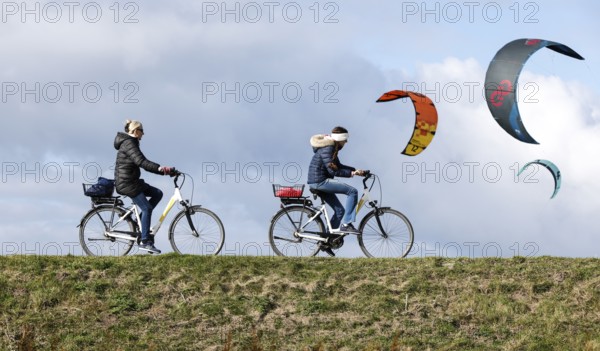 Cyclists ride across a dike and look at the sails of kite surfers, Fehmarn, 16.10.2025, Fehmarn,