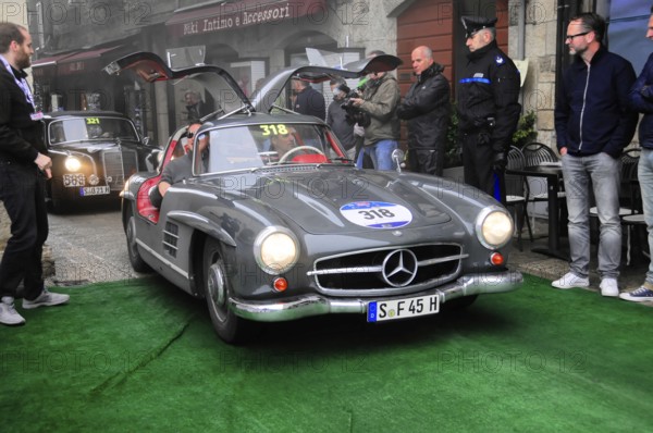 Dark gray 300 SL with open swing doors stops on the green carpet, surrounded by spectators and