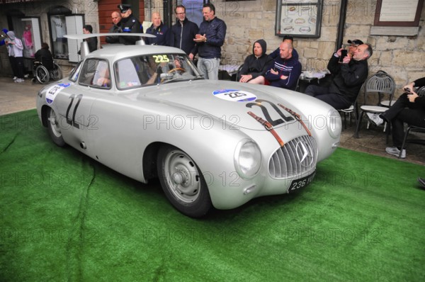 Silver Mercedes gullwing door with race number in a narrow alley at a classic car rally, spectators