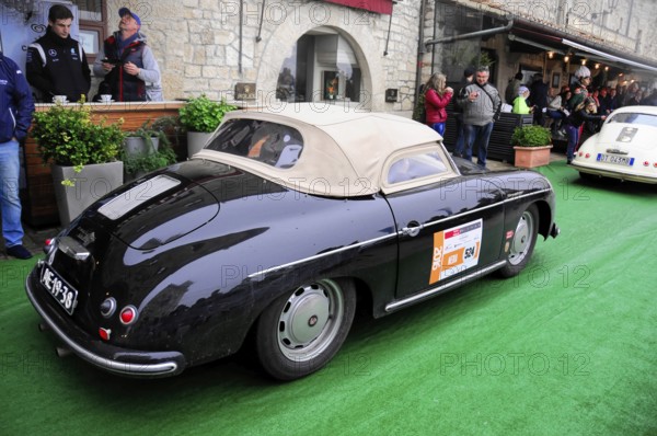Black Porsche convertible with beige soft top drives relaxed through the old town at a classic car