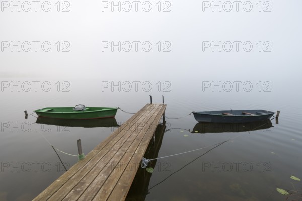 Two boats are moored on a wooden pier in fog, the atmosphere is calm and peaceful, Hopfensee,