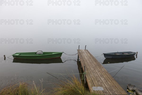 Two boats next to a wooden pier in a foggy, quiet autumn landscape, Hopfensee, Ostallgäu, Bavaria,