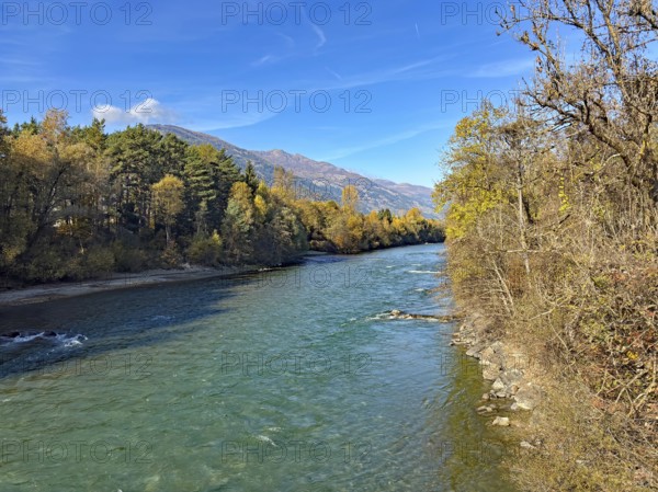 A quiet river surrounded by autumn trees and mountains under clear blue skies, Drau, Drauradweg,