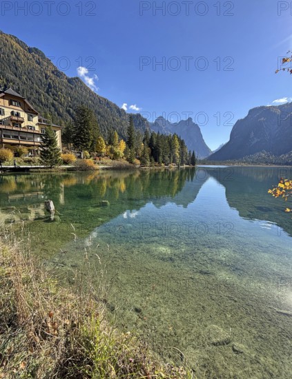 Clear water reflects the mountains and the house on the shore, Lake Toblach, Lake Dobbiaco, South