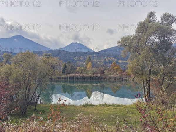 A lake in autumn surroundings, surrounded by mountains and trees under an overcast sky, Drau,
