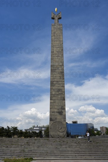 Tall stone column with symbolically decorated top under blue sky, memorial to 50 years of Soviet