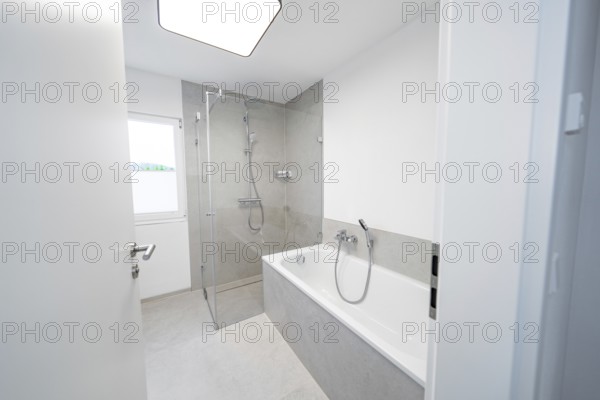 Modern bathroom with floor-level shower and tub in front of large format grey tiles and plenty of