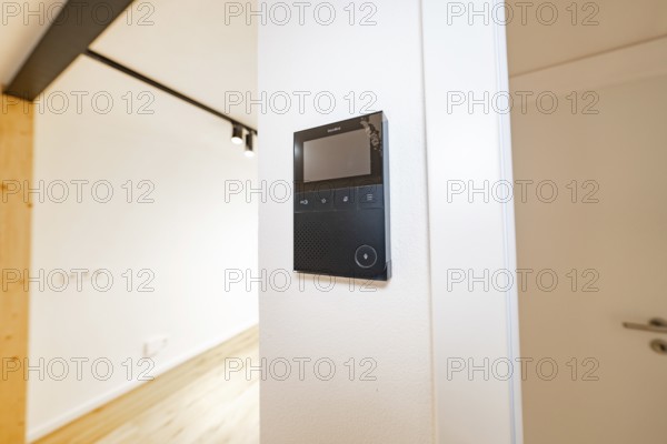 Wall intercom with display in a bright corridor next to a white door and warm parquet, house