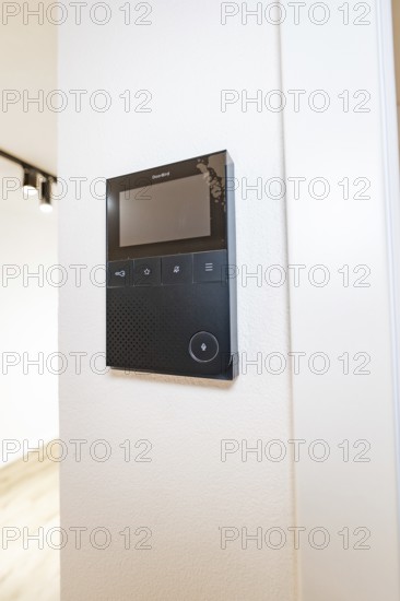 Black video intercom system with display on white wall in modern entrance area, house renovation,