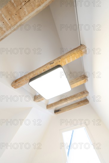 Bright room with visible wooden beams and modern ceiling light under a sloping roof, house