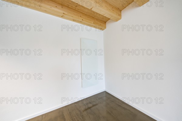 Bright corner with glass heating panel on white wall under wooden beam ceiling, reduced appearance,