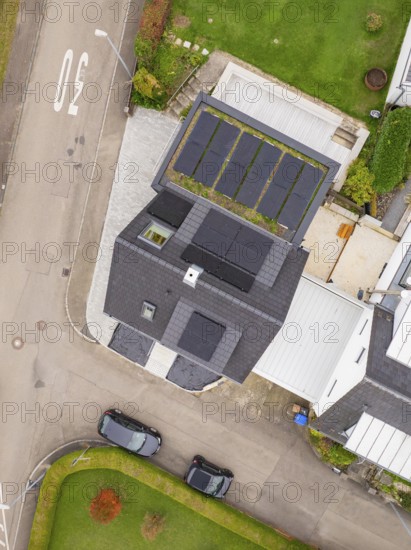 Top view of house with PV modules and carport green roof, two parked cars and curved road, house