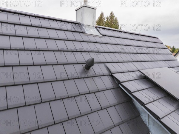 Detail of an anthracite-colored tile roof with roof vent and sheet metal connections under cloudy