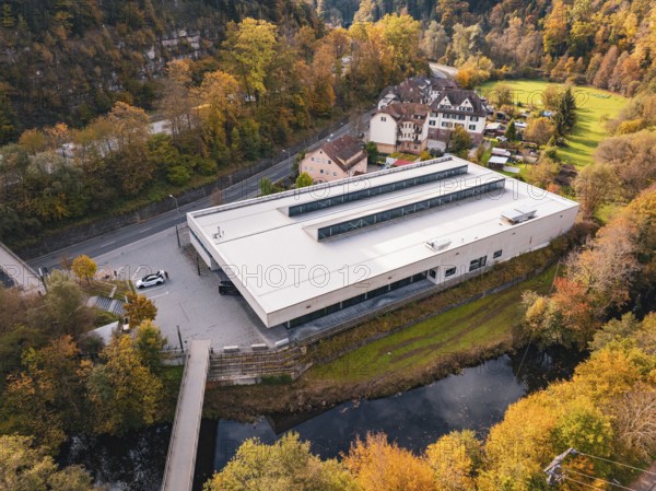 Sports hall nestled in an autumnal setting with a small river and bridge nearby, Walter Lindner