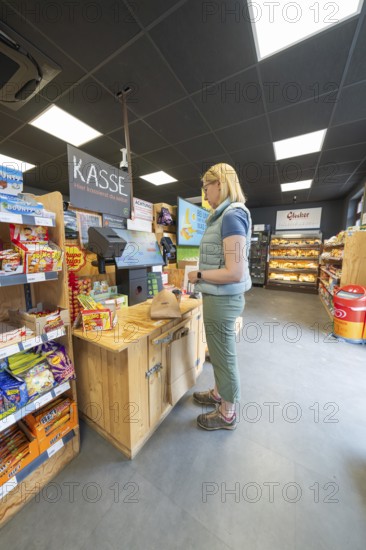 A woman stands at the cash register in a supermarket with snacks and products on the shelves, 24