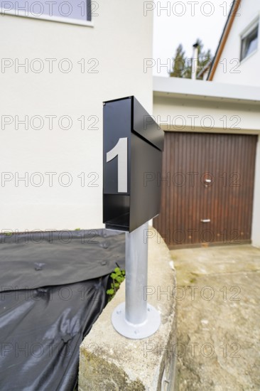 Close-up of a modern black mailbox in front of garage and plaster façade, house renovation, climate