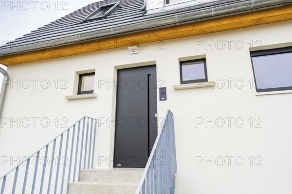 Modern house entrance with dark grey door and simple windows, staircase with metal railing, quiet